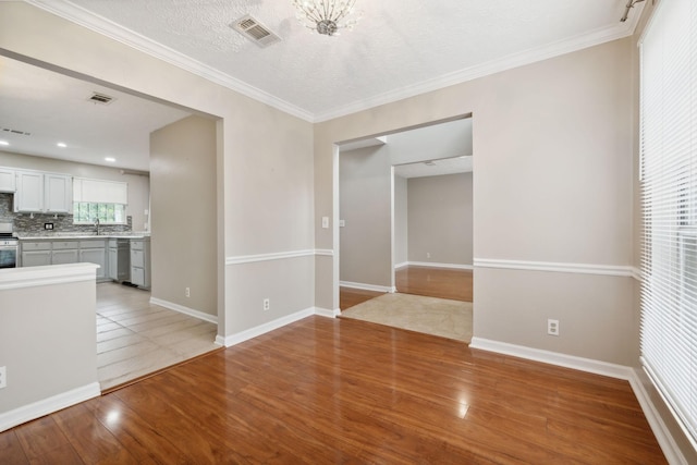 spare room featuring ornamental molding, a textured ceiling, sink, a chandelier, and light hardwood / wood-style floors