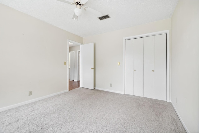 unfurnished bedroom with a textured ceiling, a closet, ceiling fan, and light colored carpet