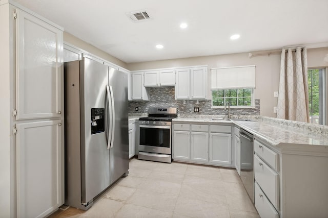 kitchen with sink, stainless steel appliances, tasteful backsplash, light stone counters, and white cabinets