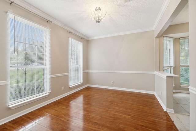 empty room featuring hardwood / wood-style floors, a notable chandelier, ornamental molding, and a textured ceiling