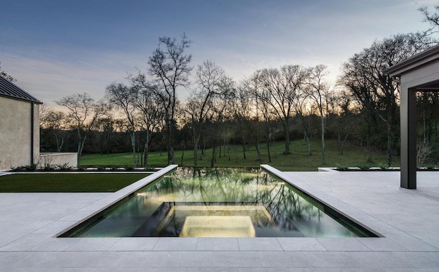 pool at dusk featuring an in ground hot tub, a yard, and a patio area