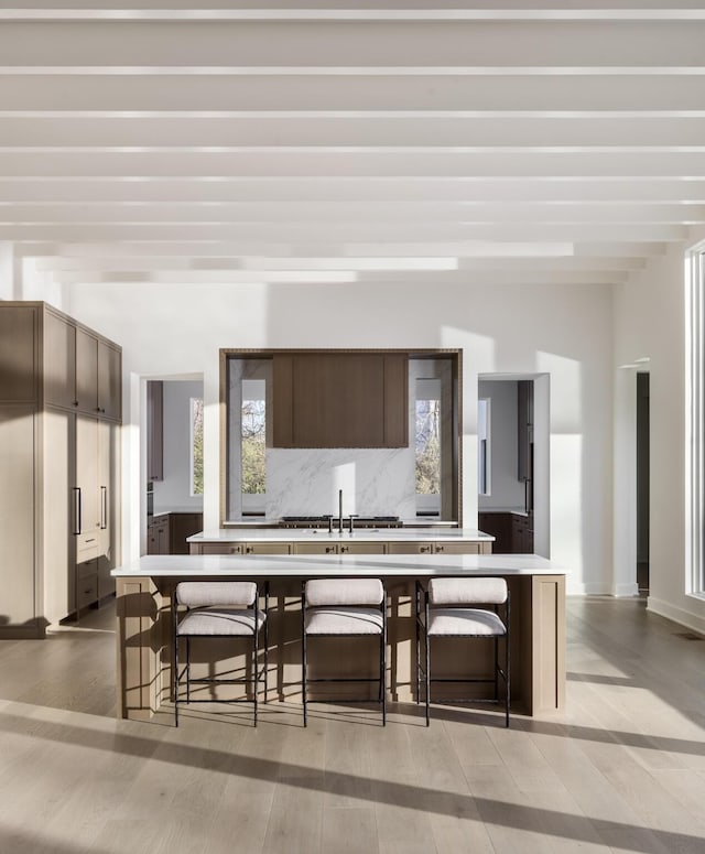 kitchen with light wood-type flooring, tasteful backsplash, dark brown cabinetry, sink, and a breakfast bar area