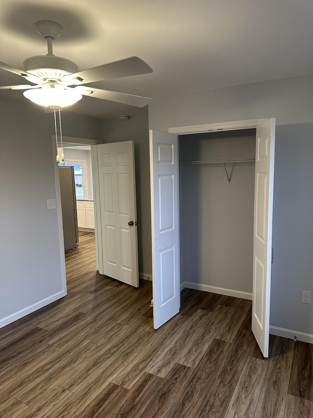 unfurnished bedroom with dark hardwood / wood-style flooring, a closet, stainless steel refrigerator, and ceiling fan