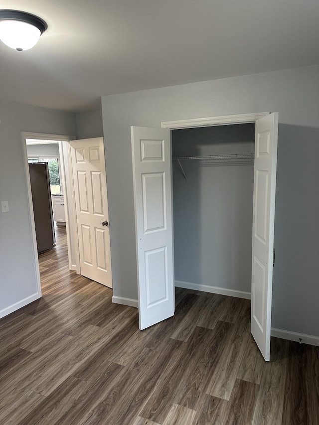 unfurnished bedroom with dark wood-style floors, a closet, and baseboards