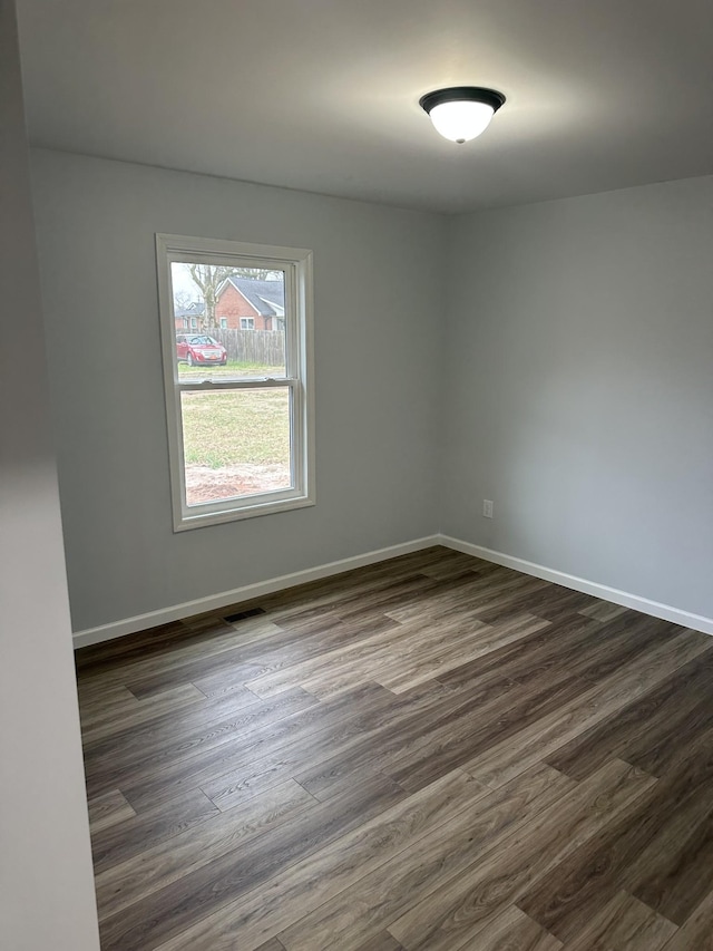 unfurnished room with dark wood finished floors, visible vents, and baseboards