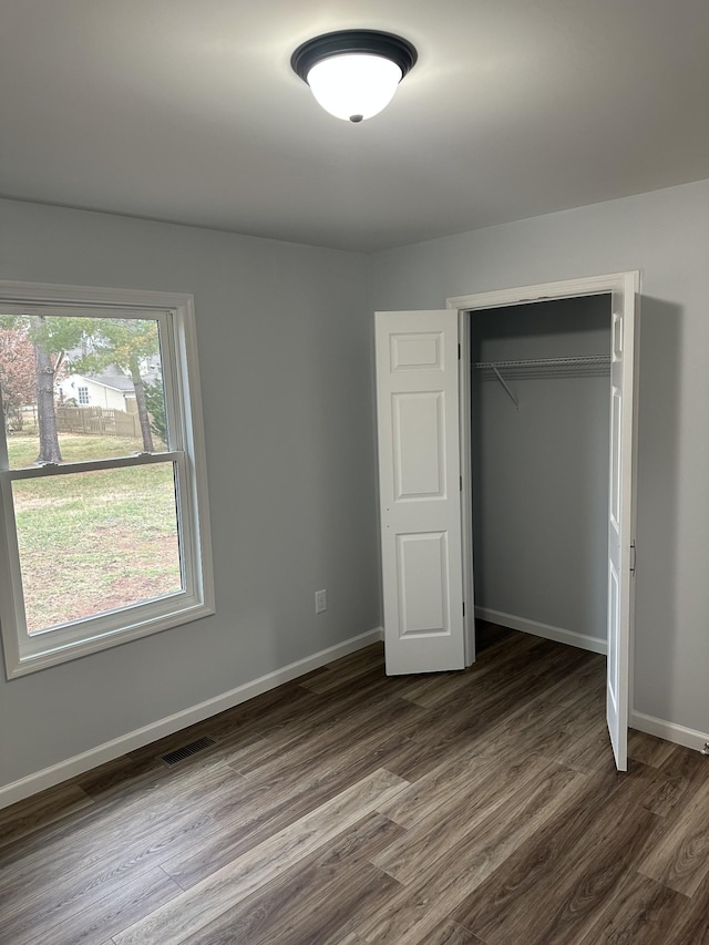 unfurnished bedroom featuring visible vents, a closet, baseboards, and dark wood-type flooring