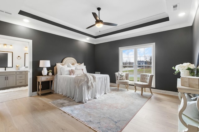 bedroom with a tray ceiling, ensuite bath, and light hardwood / wood-style flooring