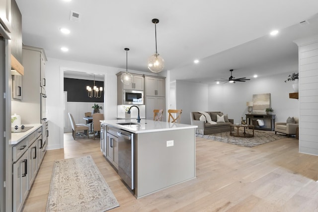 kitchen with sink, appliances with stainless steel finishes, gray cabinets, pendant lighting, and a kitchen island with sink