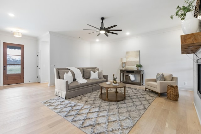 living room featuring light hardwood / wood-style flooring, crown molding, a fireplace, and ceiling fan