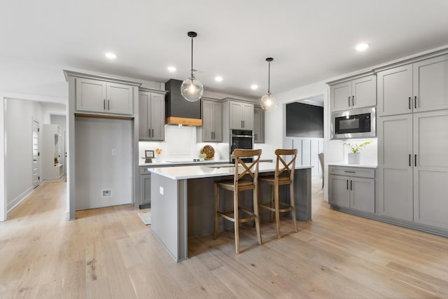 kitchen featuring pendant lighting, gray cabinets, appliances with stainless steel finishes, custom range hood, and a kitchen island