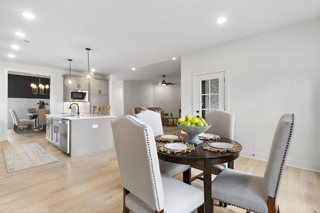 dining space featuring sink, ceiling fan with notable chandelier, and light wood-type flooring