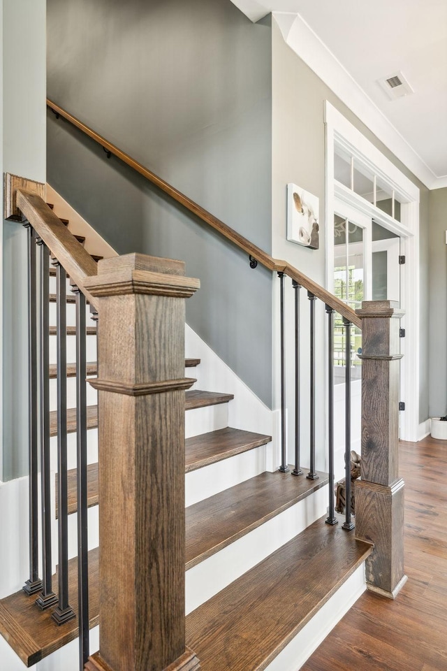 staircase with wood-type flooring and ornamental molding