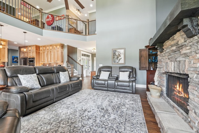 living room with a towering ceiling, ornamental molding, ceiling fan, dark wood-type flooring, and a fireplace