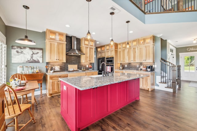 kitchen with a center island with sink, wall chimney range hood, sink, tasteful backsplash, and decorative light fixtures