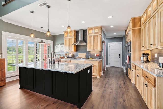 kitchen with sink, decorative light fixtures, light stone counters, and wall chimney range hood