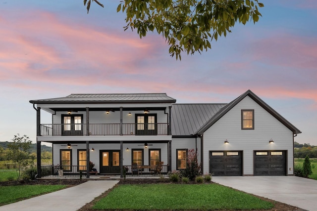 view of front of house with a balcony, ceiling fan, covered porch, a garage, and a lawn