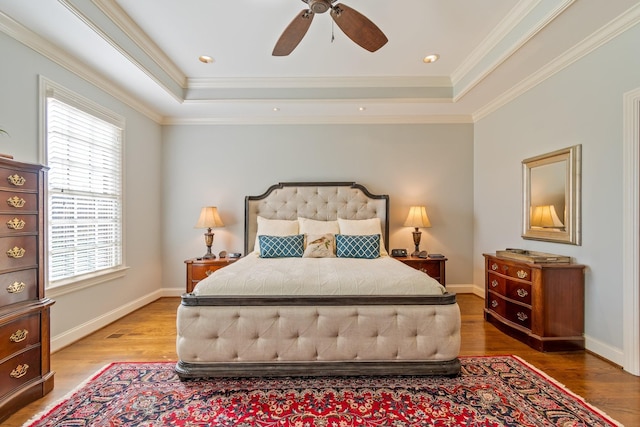 bedroom featuring hardwood / wood-style flooring, ceiling fan, ornamental molding, and a tray ceiling