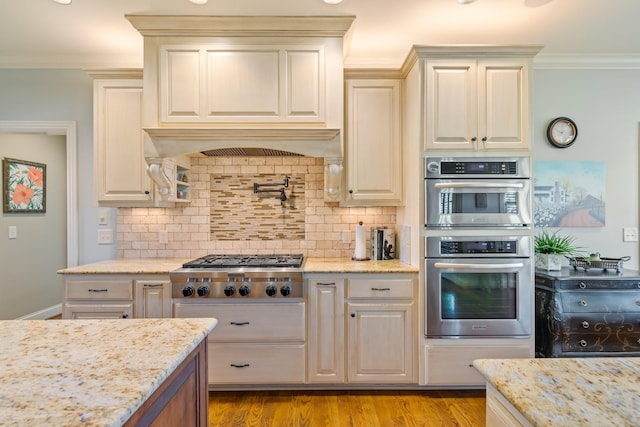 kitchen featuring crown molding, light stone countertops, tasteful backsplash, light hardwood / wood-style floors, and stainless steel appliances