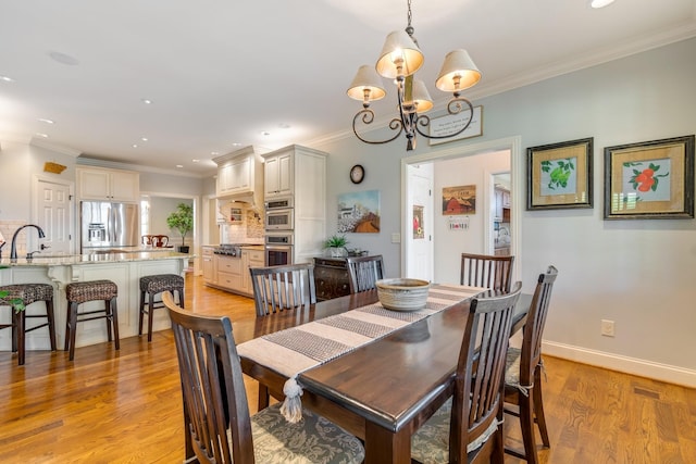 dining room featuring sink, light hardwood / wood-style flooring, ornamental molding, and a notable chandelier