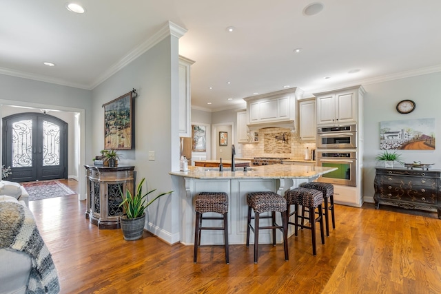 kitchen featuring kitchen peninsula, french doors, light stone counters, a breakfast bar, and white cabinetry