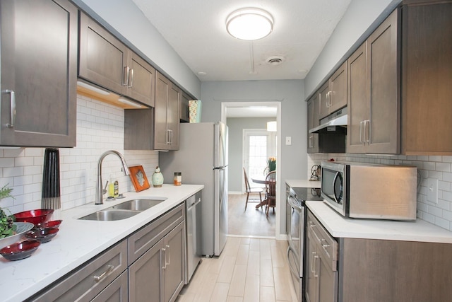 kitchen with light stone countertops, sink, backsplash, dark brown cabinets, and appliances with stainless steel finishes