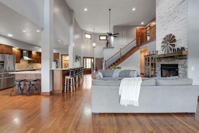 living room featuring a high ceiling, dark hardwood / wood-style floors, a stone fireplace, and ceiling fan