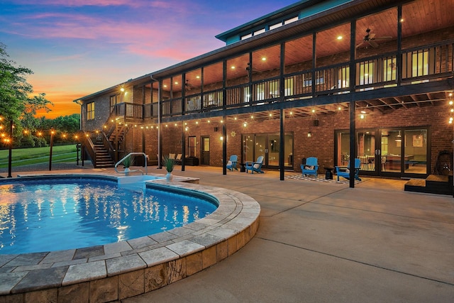 pool at dusk featuring ceiling fan and a patio