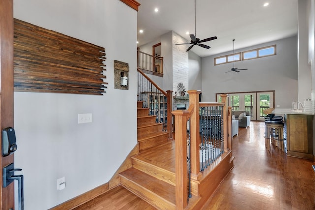 stairs featuring a high ceiling, wood-type flooring, and ceiling fan