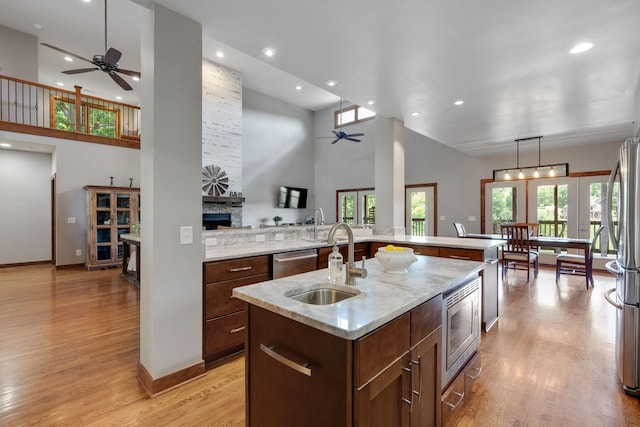 kitchen featuring sink, light hardwood / wood-style flooring, appliances with stainless steel finishes, a center island with sink, and a stone fireplace