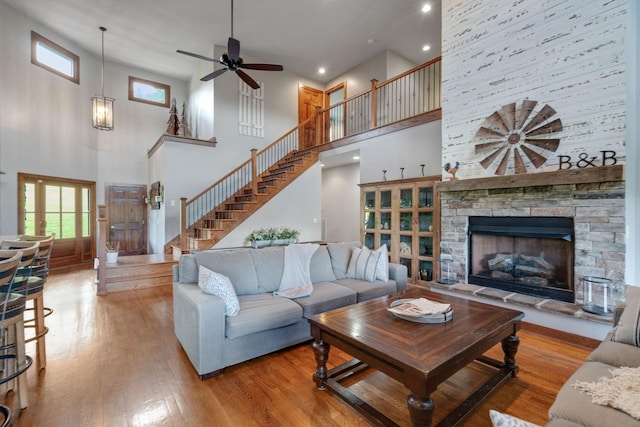 living room featuring ceiling fan, a fireplace, a high ceiling, and light hardwood / wood-style flooring