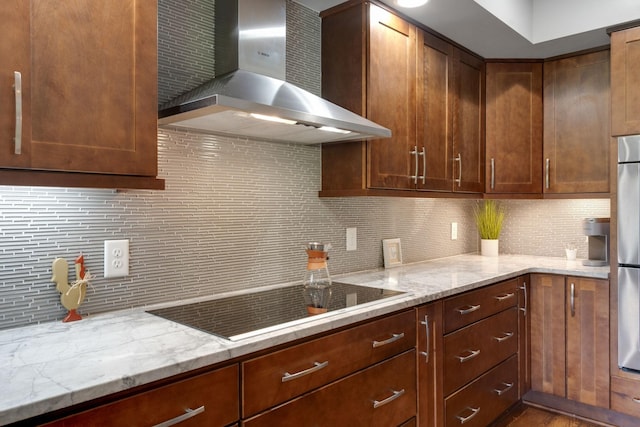 kitchen with black electric stovetop, wall chimney exhaust hood, light stone countertops, and tasteful backsplash