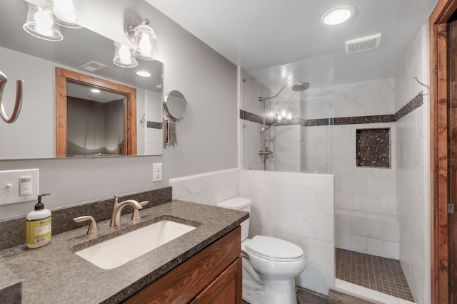 bathroom with tiled shower, vanity, toilet, and tile walls