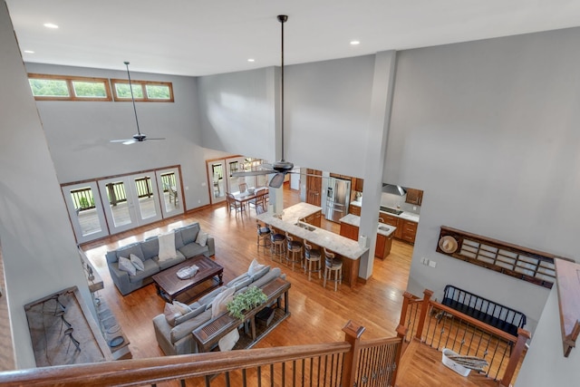 living room with ceiling fan, a towering ceiling, and light hardwood / wood-style floors