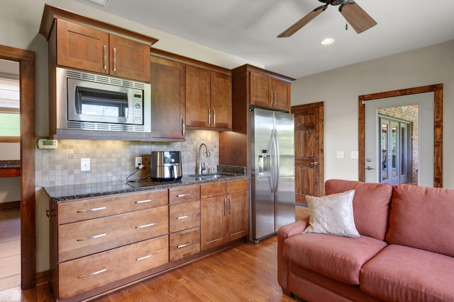 kitchen with sink, dark stone countertops, light hardwood / wood-style floors, decorative backsplash, and appliances with stainless steel finishes