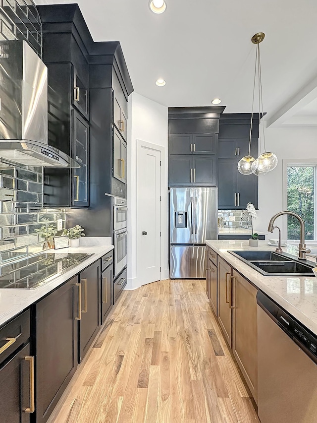 kitchen with decorative backsplash, wall chimney exhaust hood, stainless steel appliances, sink, and decorative light fixtures