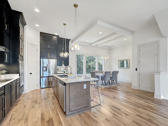 kitchen featuring appliances with stainless steel finishes, sink, pendant lighting, beamed ceiling, and an island with sink