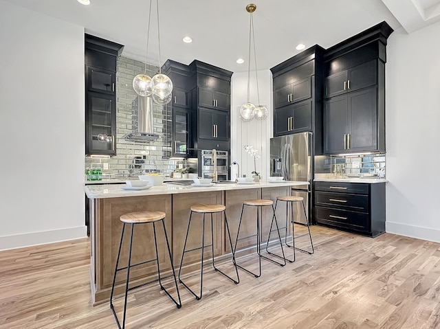 kitchen featuring appliances with stainless steel finishes, light hardwood / wood-style floors, hanging light fixtures, and an island with sink