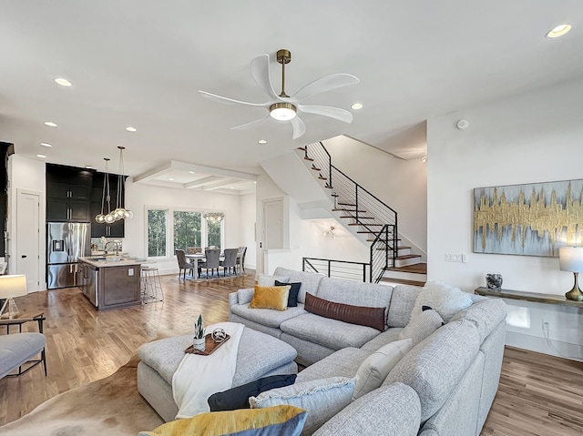 living room with ceiling fan, light hardwood / wood-style flooring, and beamed ceiling