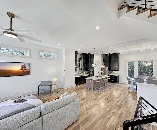 living room featuring beam ceiling, light wood-type flooring, ceiling fan, and sink