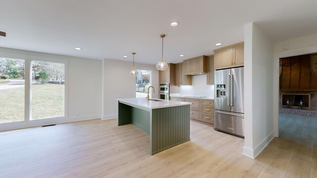 kitchen featuring appliances with stainless steel finishes, plenty of natural light, a kitchen island with sink, light hardwood / wood-style floors, and hanging light fixtures