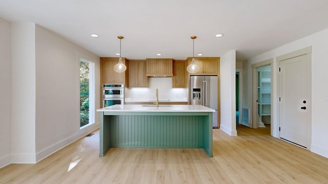 kitchen with sink, decorative backsplash, an island with sink, appliances with stainless steel finishes, and decorative light fixtures