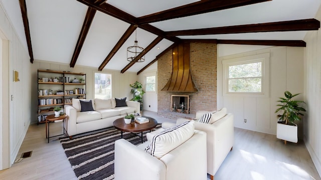 living room with a notable chandelier, vaulted ceiling with beams, light wood-type flooring, and a brick fireplace