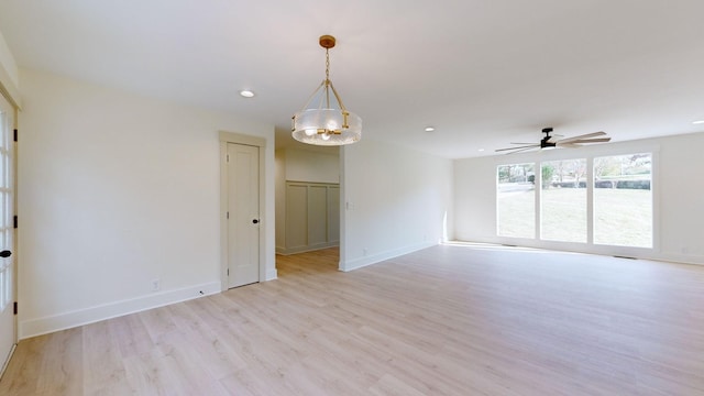 empty room featuring ceiling fan with notable chandelier and light hardwood / wood-style flooring