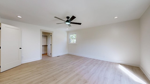 unfurnished bedroom featuring a walk in closet, ceiling fan, a closet, and light wood-type flooring