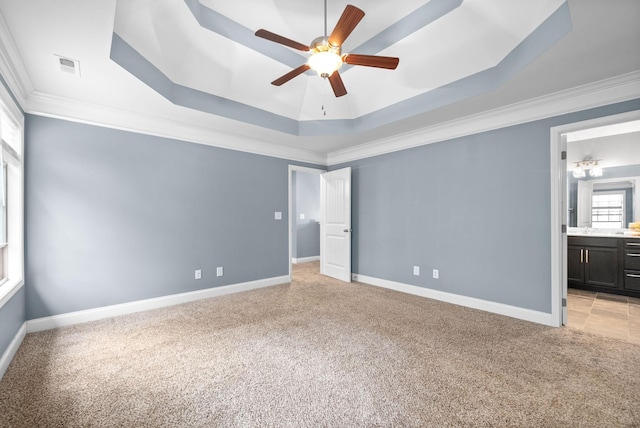 unfurnished bedroom with light carpet, ensuite bathroom, ornamental molding, a tray ceiling, and ceiling fan