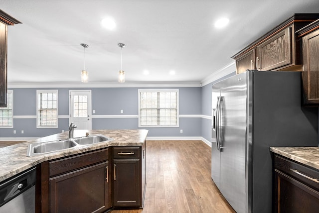 kitchen featuring pendant lighting, sink, ornamental molding, appliances with stainless steel finishes, and light hardwood / wood-style floors