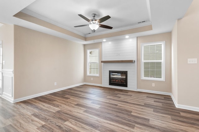 unfurnished living room with hardwood / wood-style floors, ceiling fan, a large fireplace, and a tray ceiling