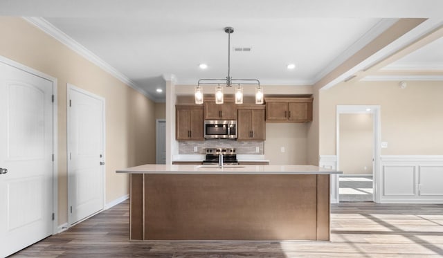 kitchen featuring crown molding, a kitchen island with sink, pendant lighting, and stainless steel appliances