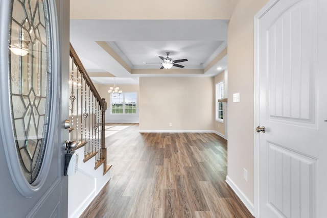 foyer entrance featuring ceiling fan with notable chandelier, a raised ceiling, crown molding, and dark wood-type flooring