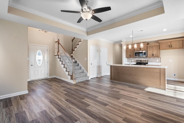 kitchen featuring decorative light fixtures, stainless steel appliances, a raised ceiling, and a kitchen island with sink